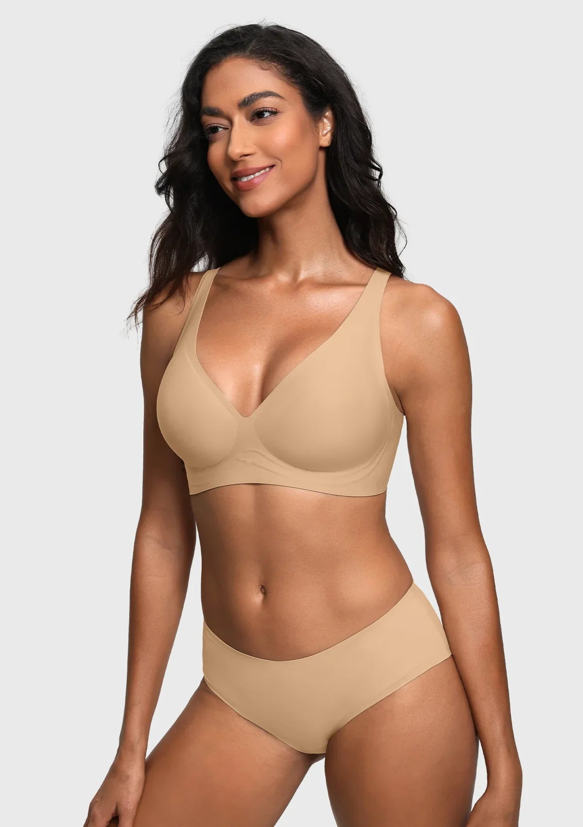 A woman modeling a matching light beige bra and high-waisted brief set against a light gray studio background.