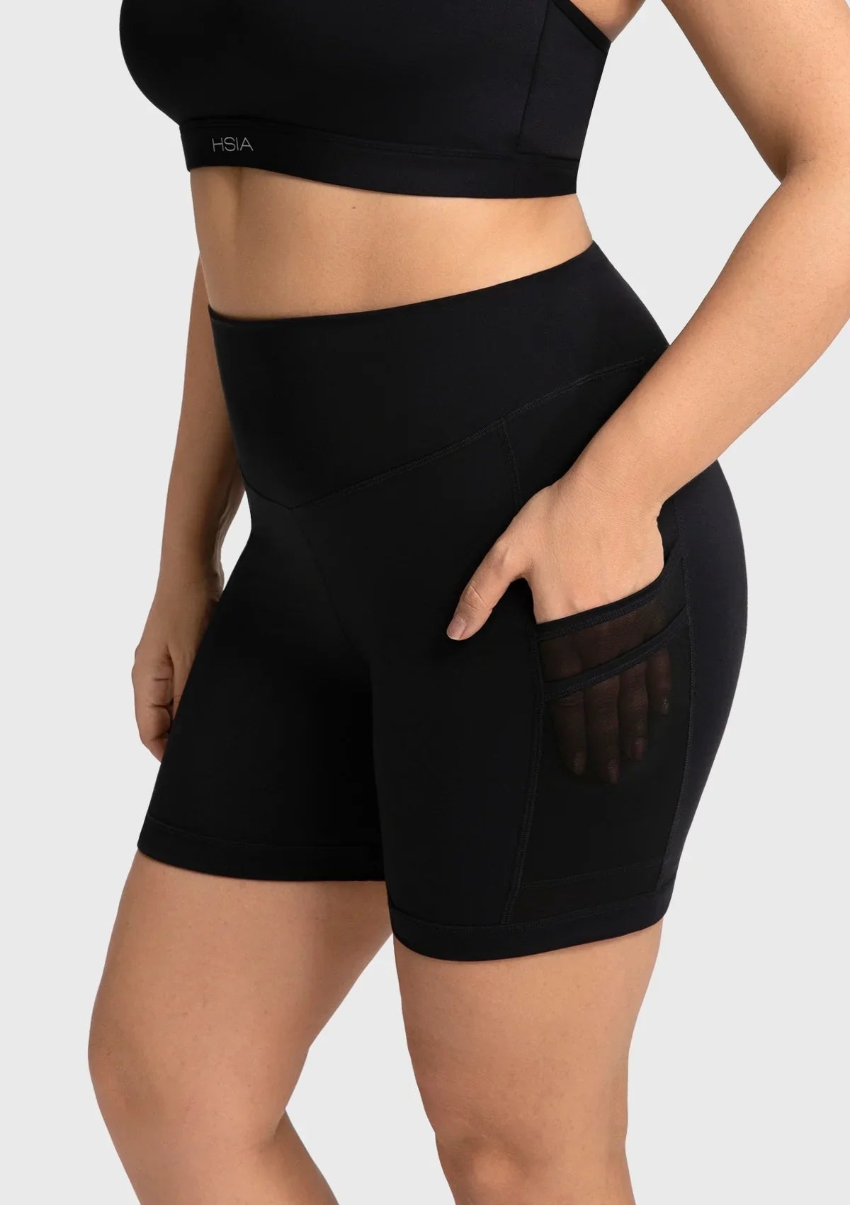 Side profile of a woman with her hands in the pockets of the black cooling workout shorts, highlighting the stylish and breathable mesh splicing.