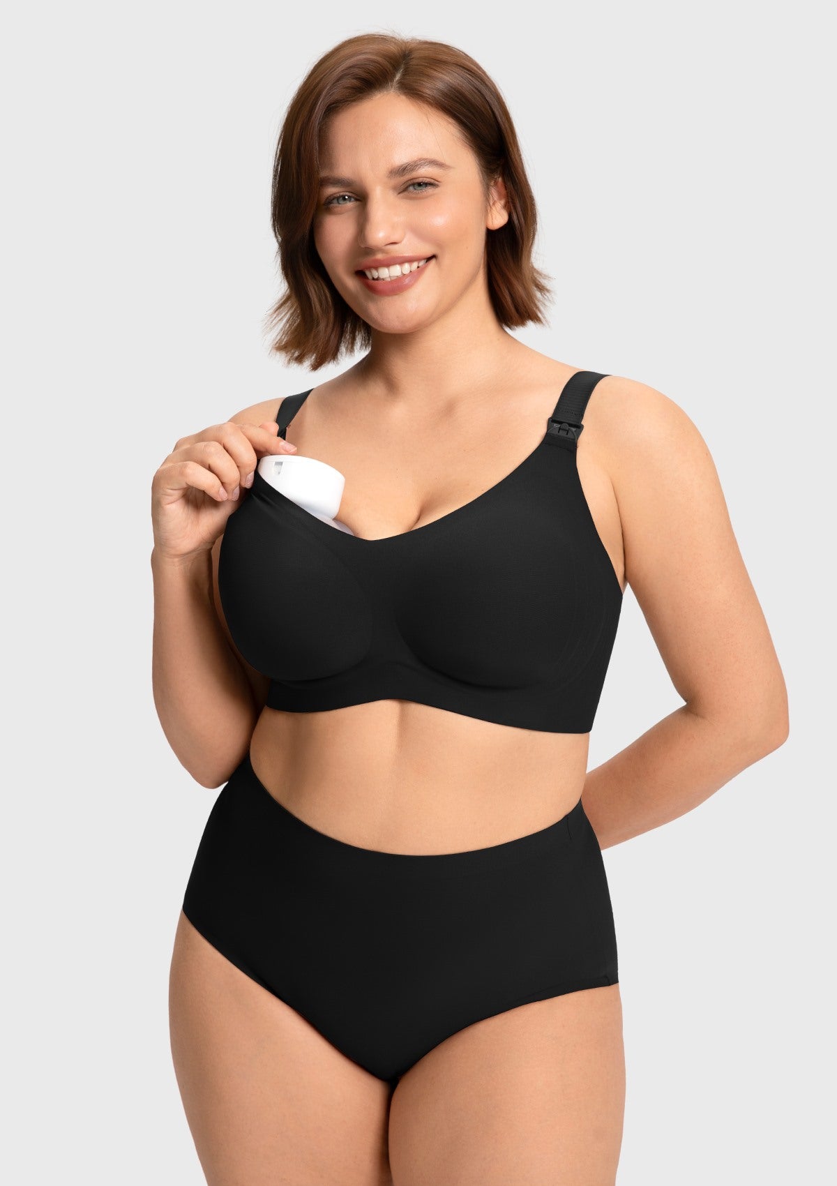 Model demonstrating hands-free pumping by securing a breast pump inside the black wireless nursing bra cup, providing convenience for multitasking moms.
