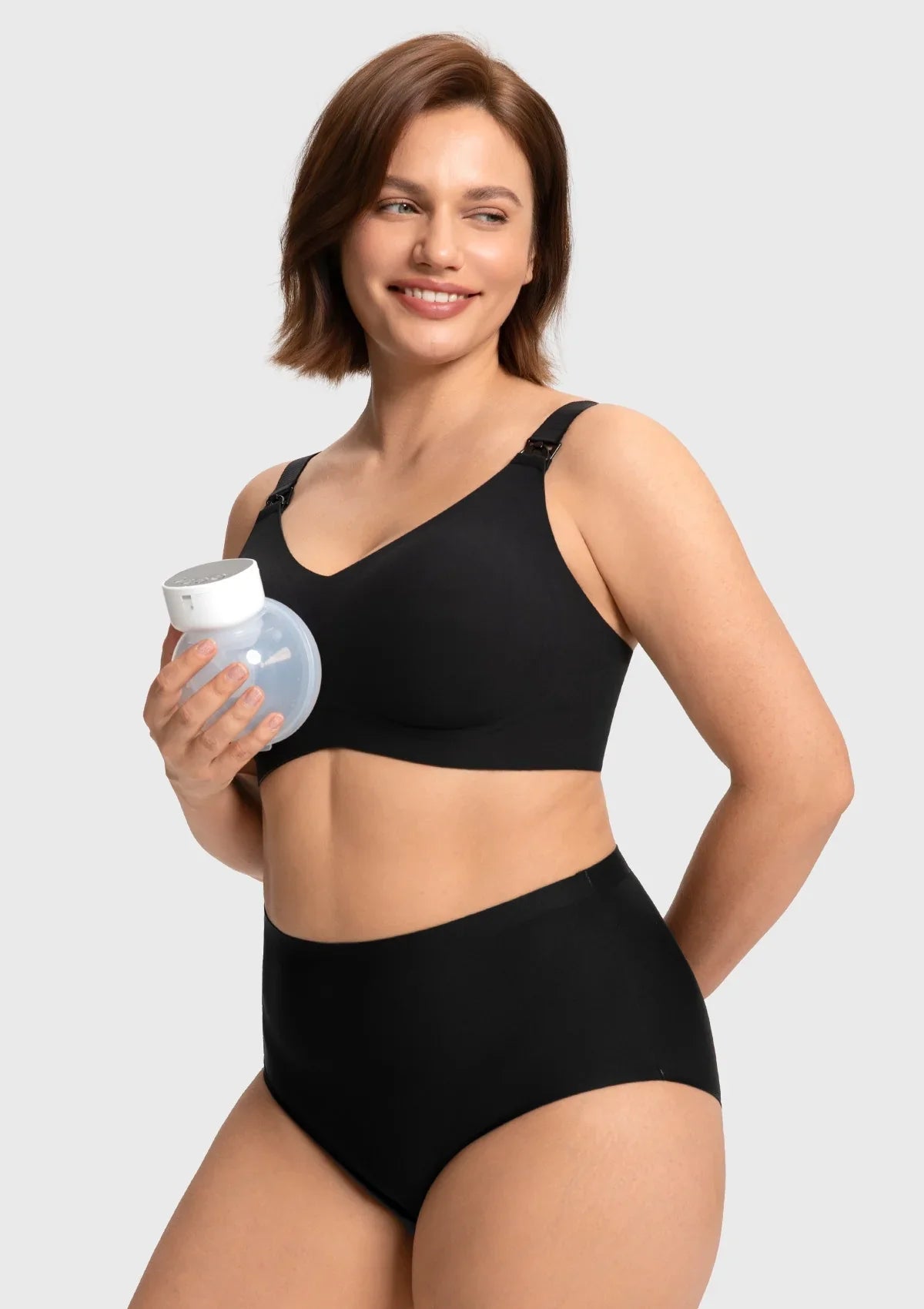 Model holding a breast pump next to the black drop-down nursing bra, showcasing the easy one-handed clip for seamless breastfeeding or pumping access.