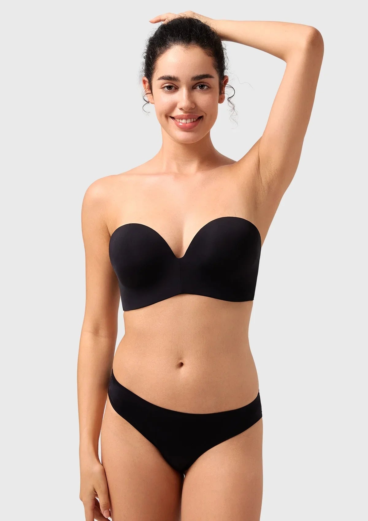 Smiling woman lifting her arms to show the absolute secure, non-slip fit of the black best strapless bra.