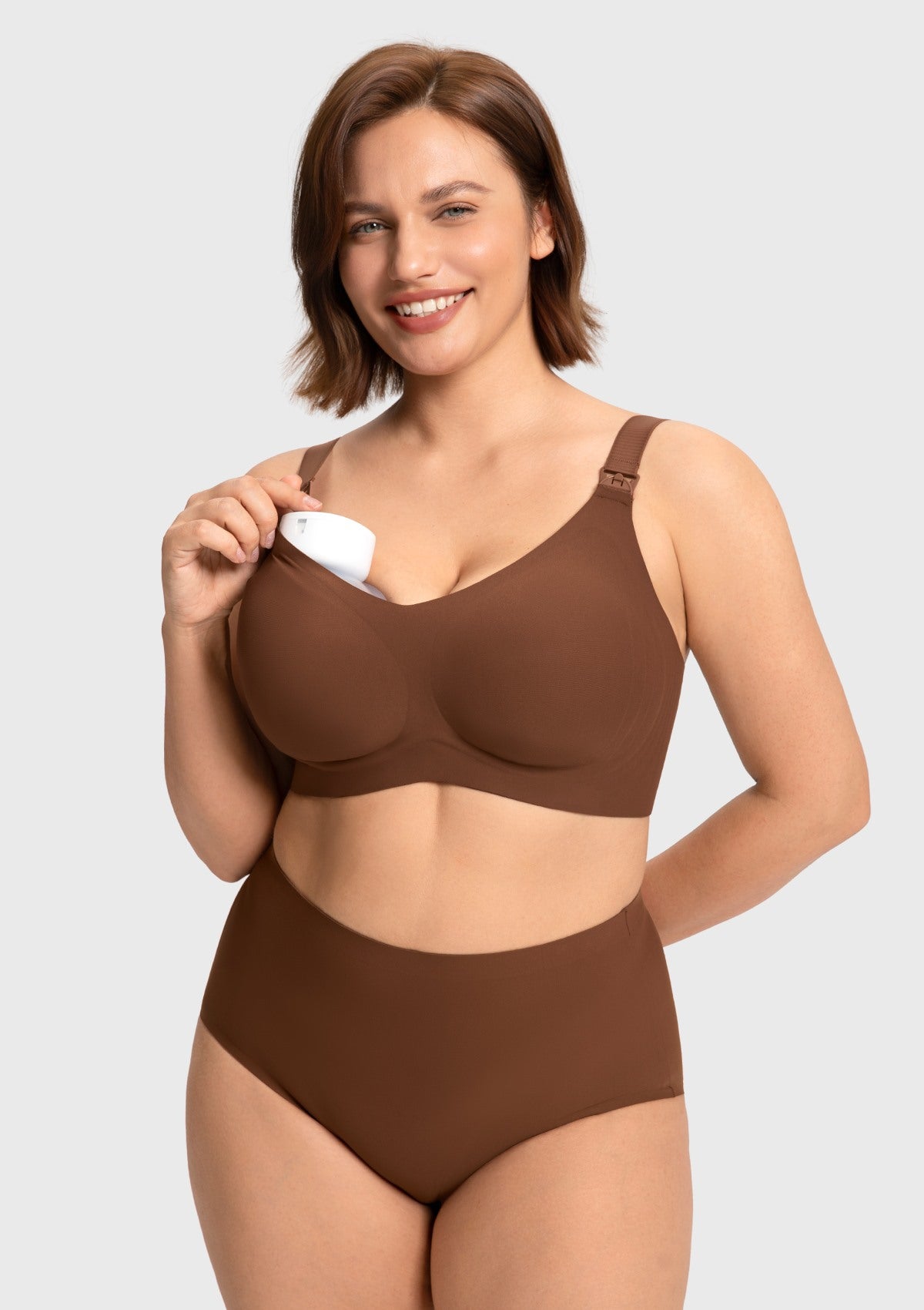 Model holding a breast pump within the cocoa brown supportive nursing bra cup, illustrating the stable hands-free pumping capability for active moms.