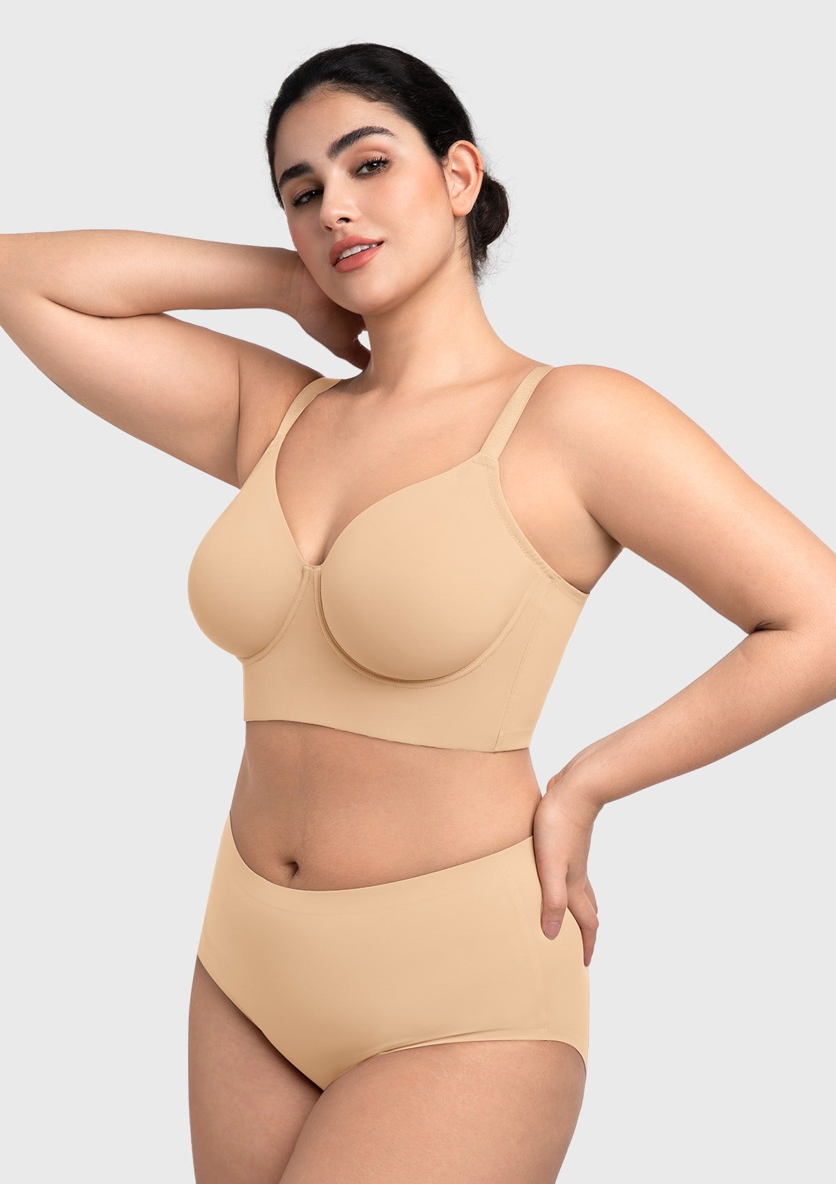 Side view with arms raised in the beige Delia bra, emphasizing the wide elastic underband that prevents rolling.