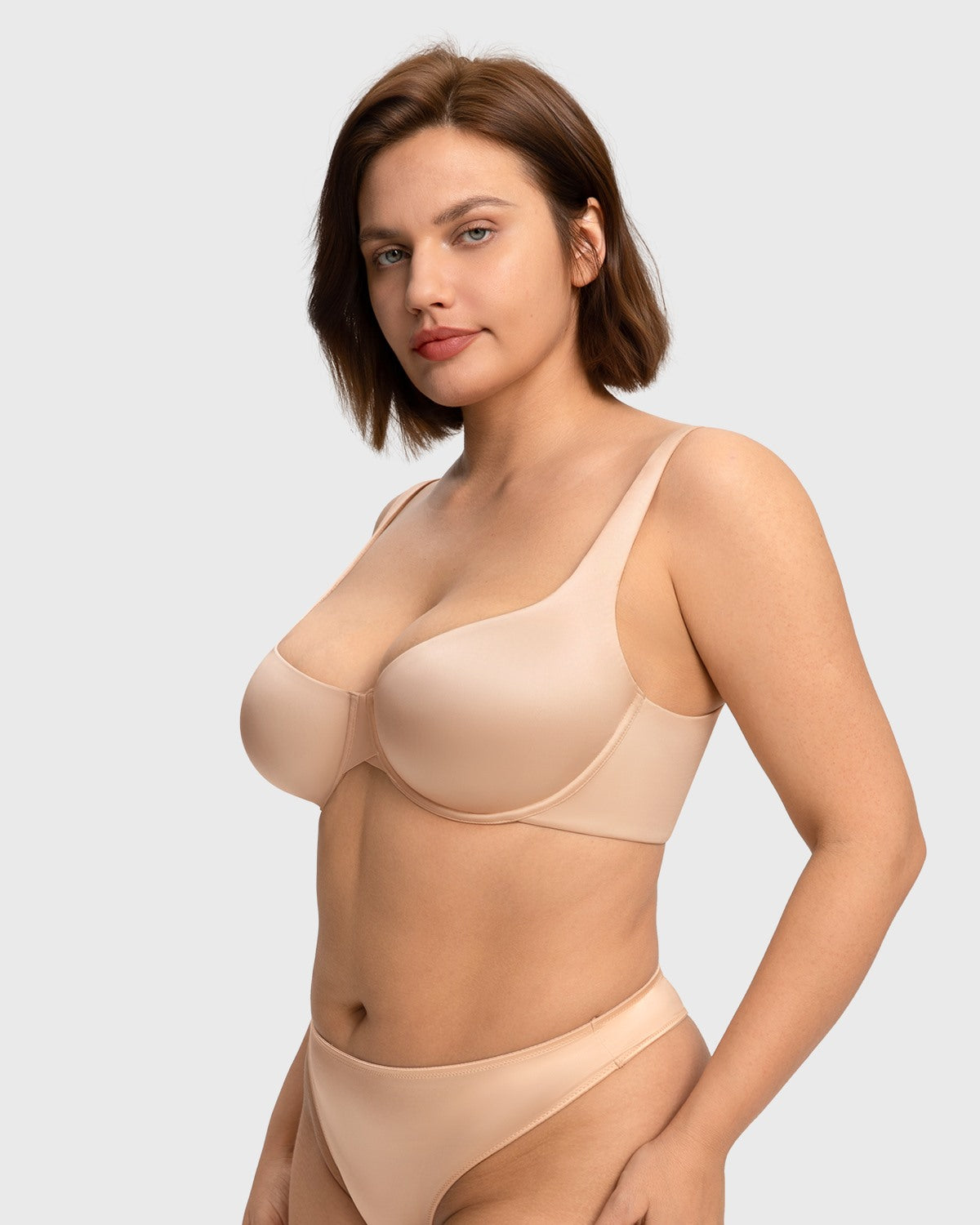 Confident woman with hands on hips wearing the light beige seamless balconette bra, highlighting the flattering criss-cross center gore and second-skin fit.
