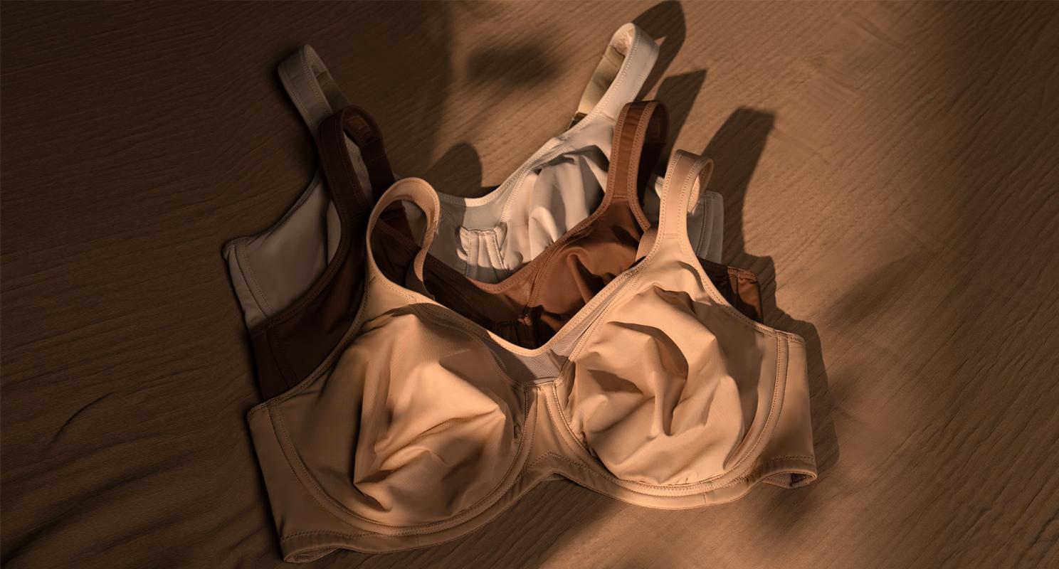 Three supportive bras in nude, brown and white flat lay on warm wood surface, showing everyday comfortable options for large busts