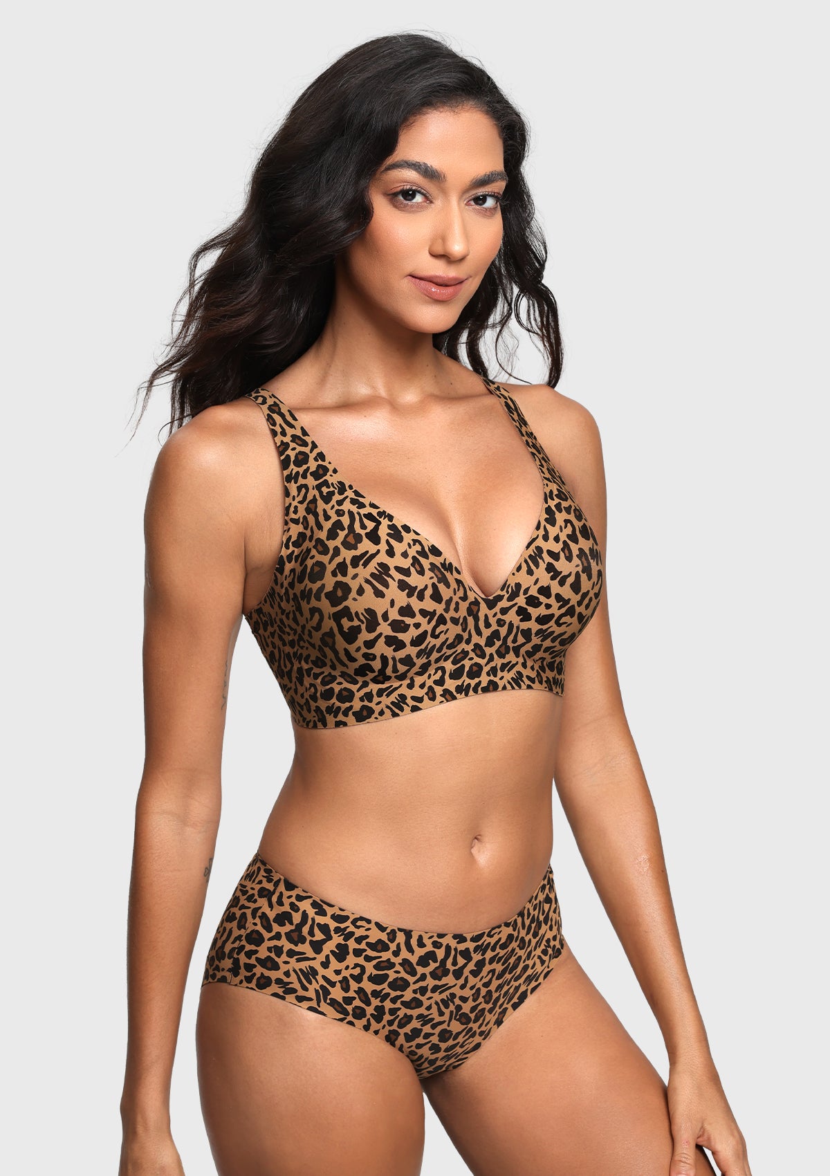 A woman modeling a leopard-print two-piece bikini set against a light gray studio background. The set features a triangle-style bra top and matching high-waisted briefs in a brown, black, and tan animal print pattern.