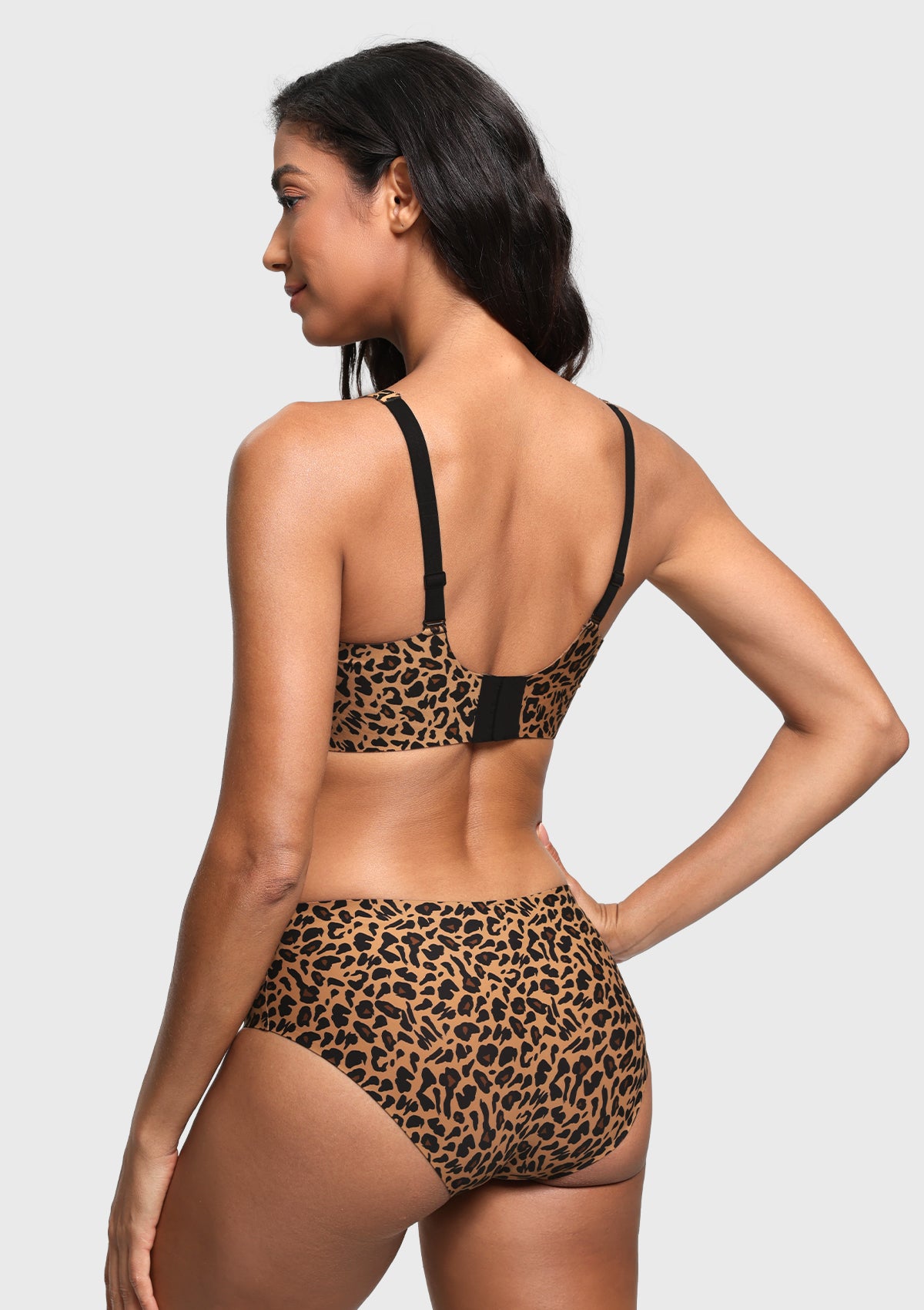 A woman shown from the back wearing a leopard-print two-piece swimsuit with black straps, against a light gray studio background.