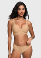 A woman modeling a light beige wireless bra and matching high-waisted briefs against a light gray studio background.