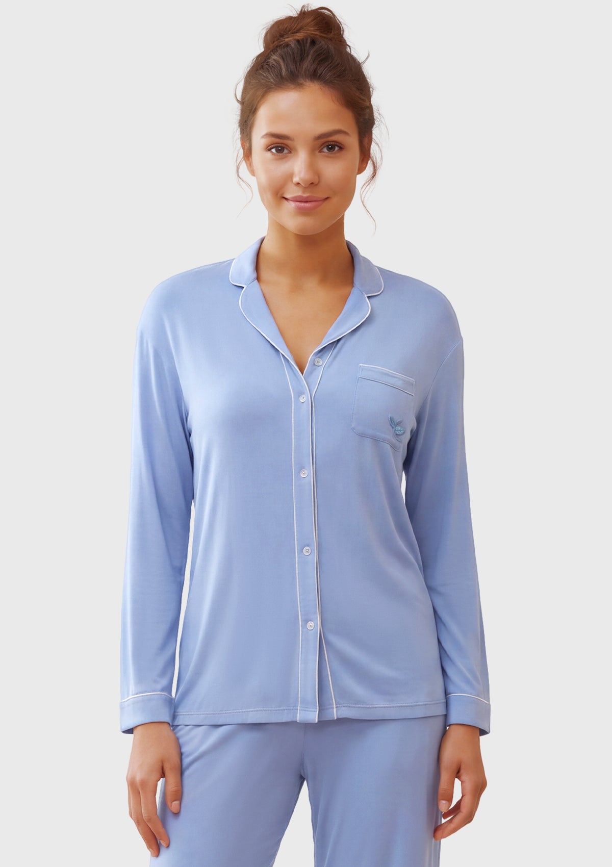 A woman modeling a light blue long-sleeve pajama set with a button-front top and matching pants against a plain light gray studio background.