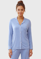 A woman modeling a light blue long-sleeve pajama set with a button-front top and matching pants against a plain light gray studio background.