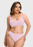 A woman modeling a light pink two-piece bikini set against a plain light gray studio background.