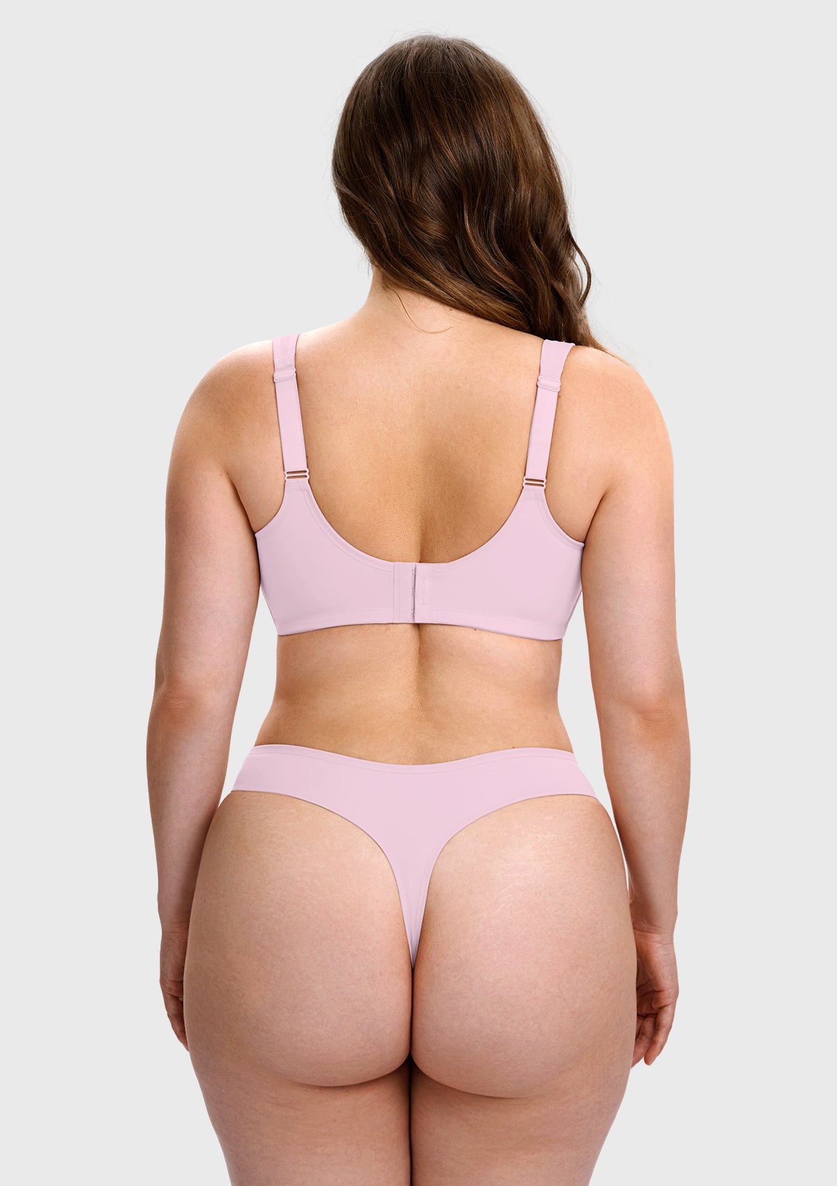 A woman shown from the back wearing a light pink two-piece lingerie set, consisting of a bralette with adjustable shoulder straps and matching high-cut thong bottoms, against a solid light gray background.