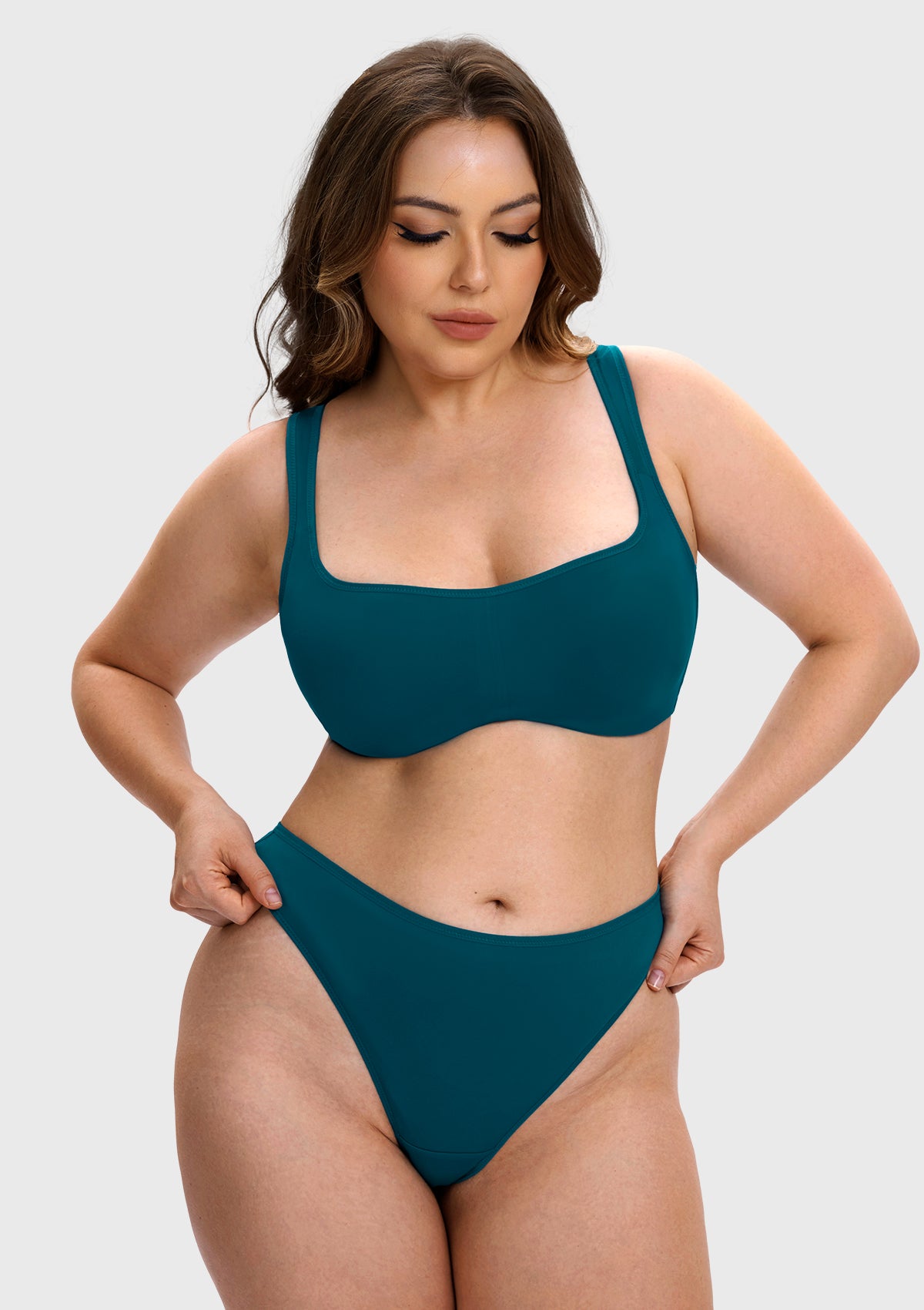 A woman modeling a solid teal two-piece bikini set against a light gray studio background.