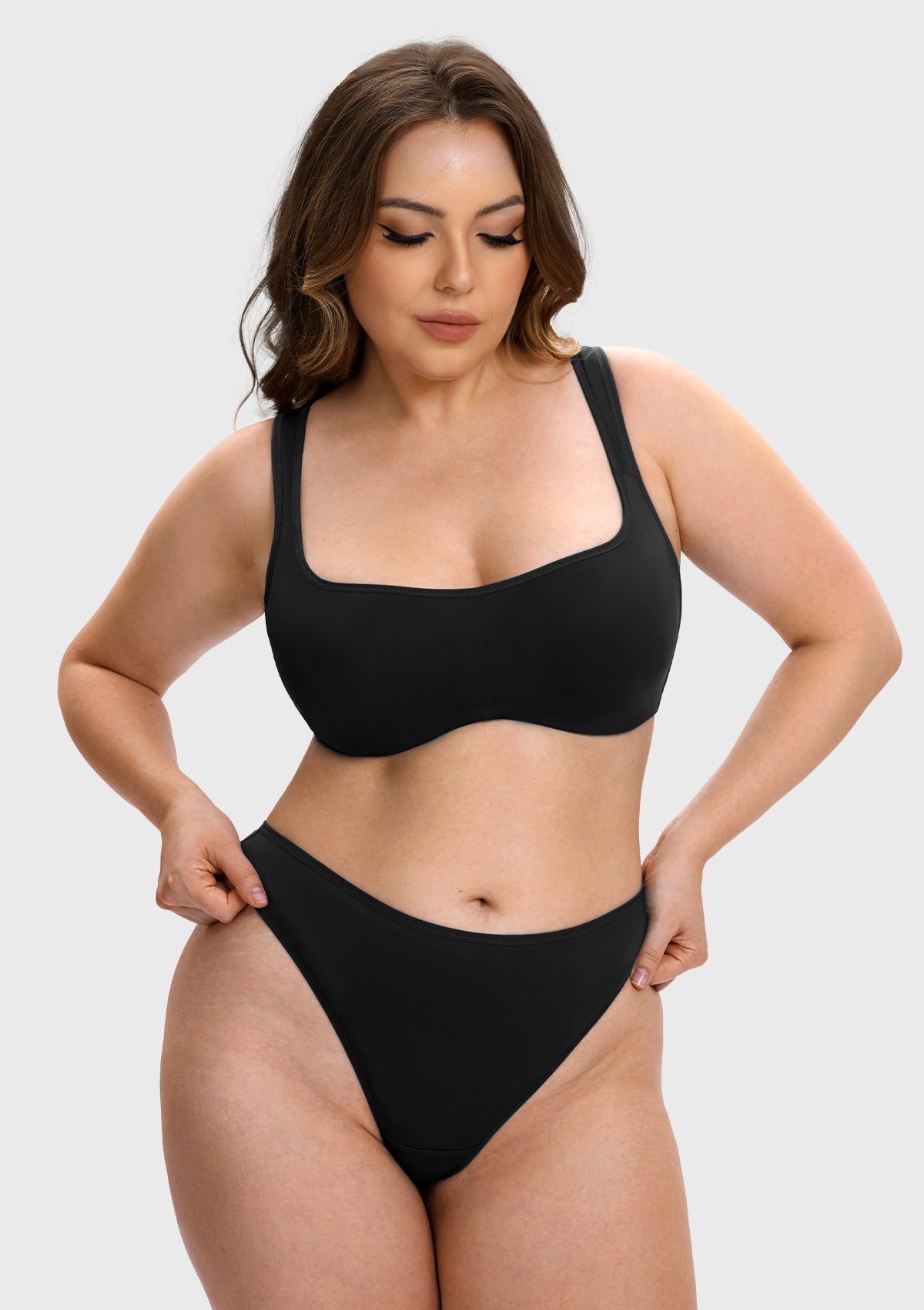 A woman modeling a solid black two-piece bikini set against a light gray studio background.