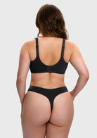 A woman shown from the back wearing a black bra and matching thong underwear against a light gray studio background.
