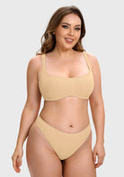A woman modeling a two-piece beige bikini set against a light gray studio background. The set includes a scoop-neck bra top and matching high-cut bottoms.